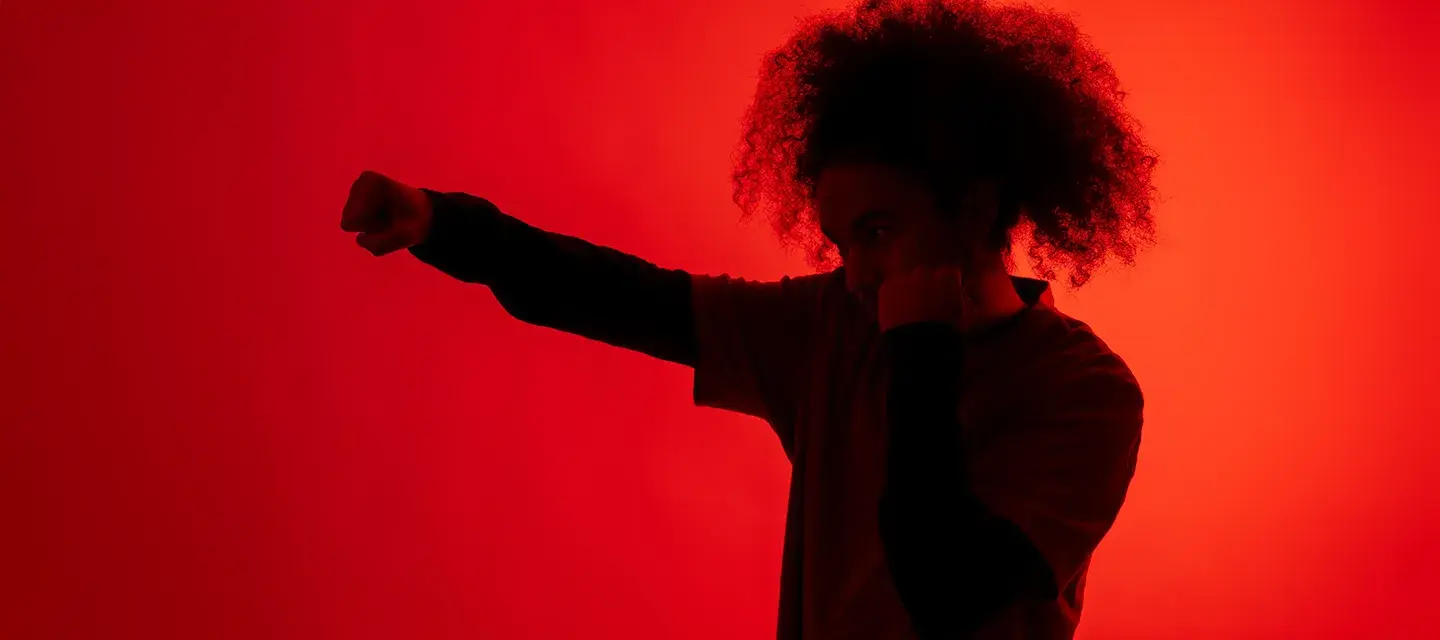 A shadow of a man with afro hair throwing a punch under red light